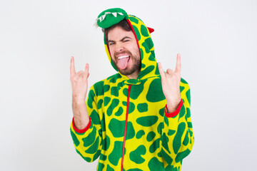 Young caucasian man wearing a pajama standing against white background making rock hand gesture and showing tongue