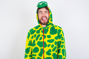 Young caucasian man wearing a pajama standing against white background showing grimace face crossing eyes and showing tongue. Being funny and crazy