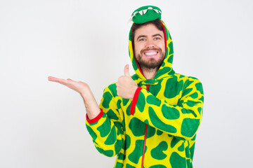 Fototapeta premium Young caucasian man wearing a pajama standing against white background Showing palm hand and doing ok gesture with thumbs up, smiling happy and cheerful.