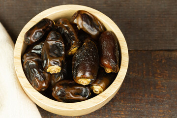 Close-up dried dates palm in wooden bowl with cloth on wooden background.