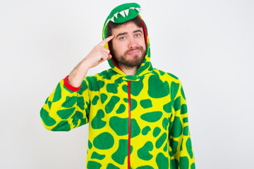 Fototapeta premium Young caucasian man wearing a pajama standing against white background tries to memorize something, keeps fore finger on temple, reminds information for exam,