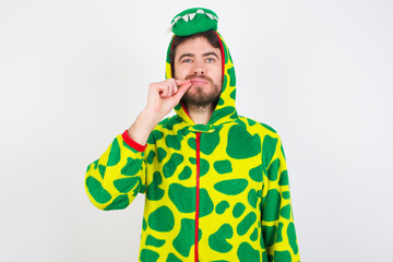 Fototapeta premium Young caucasian man wearing a pajama standing against white background mouth and lips shut as zip with fingers. Secret and silent, taboo talking.