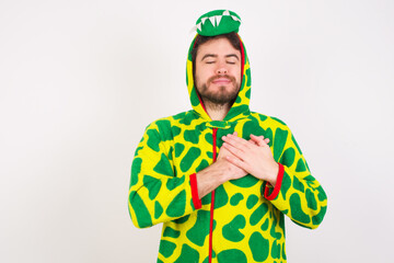Young caucasian man wearing a pajama standing against white background smiling with hands on chest with closed eyes and grateful gesture on face. Health concept.