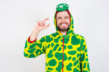 Young caucasian man wearing a pajama standing against white background smiling and confident gesturing with hand doing small size sign with fingers looking and the camera. Measure concept