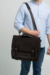 Brown men's shoulder leather bag for a documents and laptop on the shoulders of a man in a blue...
