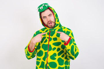 Embarrassed Young caucasian man wearing a pajama indicates at herself with puzzled expression, being shocked to be chosen to participate in competition, hesitates about something