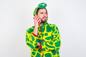 Fototapeta premium Sad Young caucasian man wearing a pajama standing against white background talking on smartphone. Communication concept.