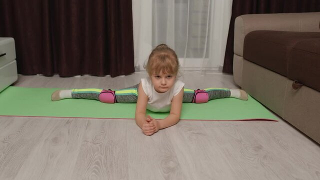 Fit little child kid training gymnastics fitness twine stretching workout on mat. Healthy lifestyle, active leisure at home. Children girl in sportswear making sport exercises, warming up cardio