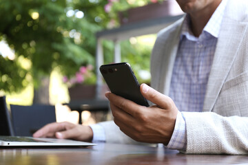 Businessman with smartphone in outdoor cafe, closeup
