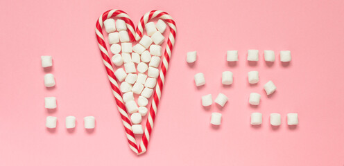 White-red candy canes and marshmallow in heart shape and love on pink background. Concept of love, happy valentine's day, women's day, christmas and birthday celebration. Flatly, copy space, mock up