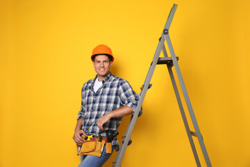 Professional builder near metal ladder on yellow background - obrazy, fototapety, plakaty
