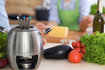 Fondue in a pot at the background of friends cooking together, close-up. Kitchen interiors and cookware