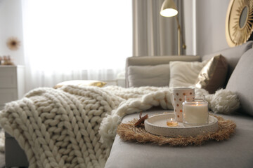 Cup of drink and burning candles on sofa in room, space for text. Interior elements