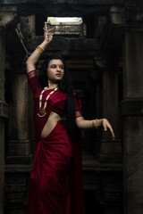 Portrait of beautiful Indian girl in heritage stepwell wearing traditional Indian red saree, gold...