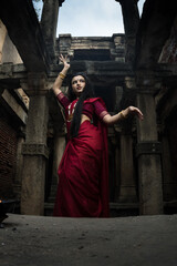 Portrait of beautiful Indian girl in heritage stepwell wearing traditional Indian red saree, gold...