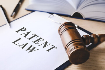 Clipboard with phrase Patent Law and gavel on wooden table, closeup