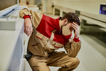 Factory worker with face mask feeling ill and holding his head in pain at production facility.