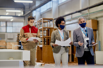 Quality control inspectors communicating while walking through woodworking facility during...