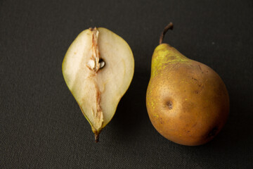 whole and half fruit of a yellow-green pear on a dark background