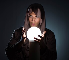 Young wizard with crystal ball in dark room