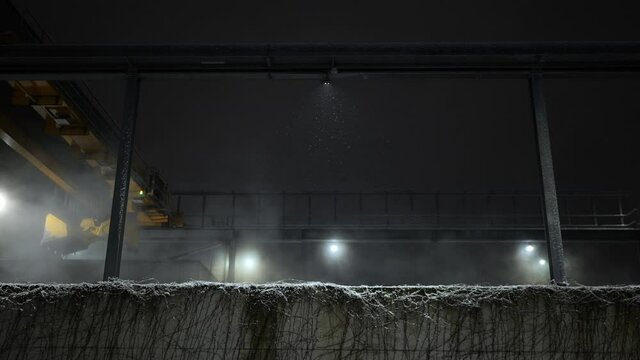 Automatic industrial grab crane working during cold night while it's snowing and steam coming off material clamshell grab bucket