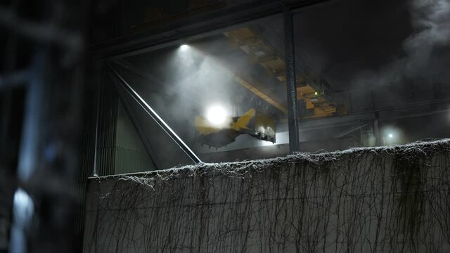 Closer shot of running industrial grab crane during cold winter night with snow falling down and steam coming off