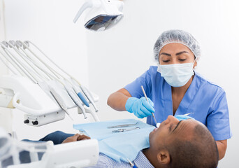 Dentist in uniform is examinating man on the chair