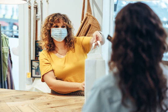 Clothing store owner with face mask assisting customer