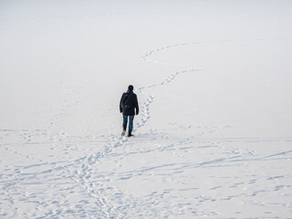 A man in a black jacket with a backpack walking on snow, footprints in snow, behind