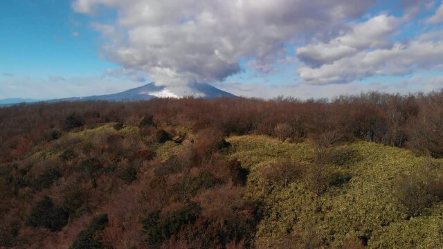 Aerial upward reveal of Mount Fuji and Gotemba city behind hill on cloudy day