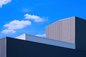 Low angle and perspective side view of corrugated metal factory buildings in modern style against blue sky background