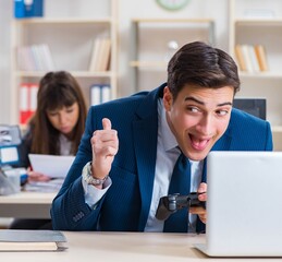 Man playing games in office while colleague is busy
