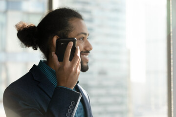 Smiling millennial African American businessman hold modern smartphone listen to audio message on loudspeaker. Happy male employee use digital voice assistant on cellphone. Technology concept.