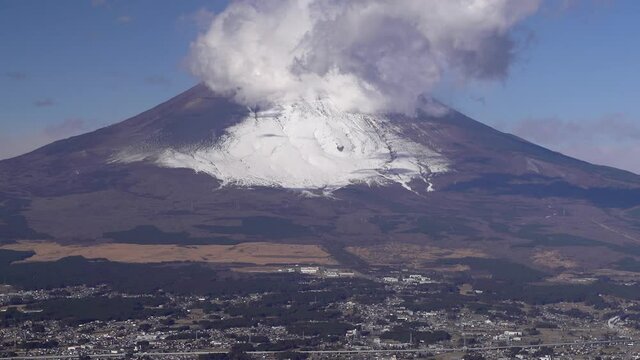 Slow tilt up over Gotemba city at bottom of snowy Mount Fuji on clear day