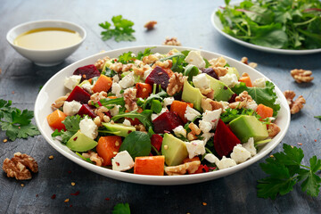 Healthy Butternut squash salad with beetroot, avocado, walnut and feta cheese in white bowl