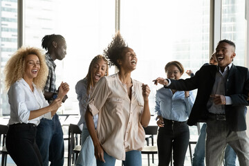 Naklejka premium Overjoyed diverse multiracial colleagues have fun dancing together at office party. Happy multiethnic employees feel excited joyful celebrate Friday or weekend at workplace. Celebration concept.