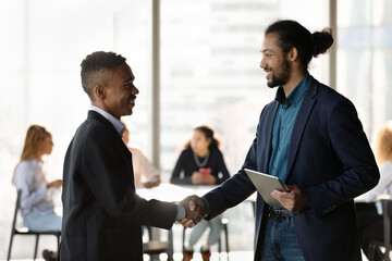 Smiling African American boss or CEO handshake excited ethnic male employee congratulate with...