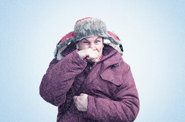 A man in red winter clothes wipes his nose with his hand in the cold, snow is falling around