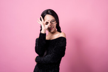 Fototapeta premium Happy cheerful young woman wearing her black hair rejoicing at positive news or birthday gift, looking at camera with joyful and charming smile. Asian girl portrait on pink background in studio