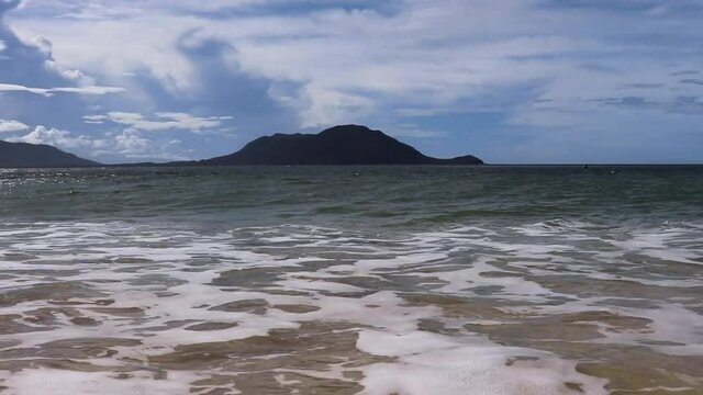 Establishing shot at Nudey beach in Australia on Fitzroy Island. Beautiful view of waves coming in with a mountain in full view. 