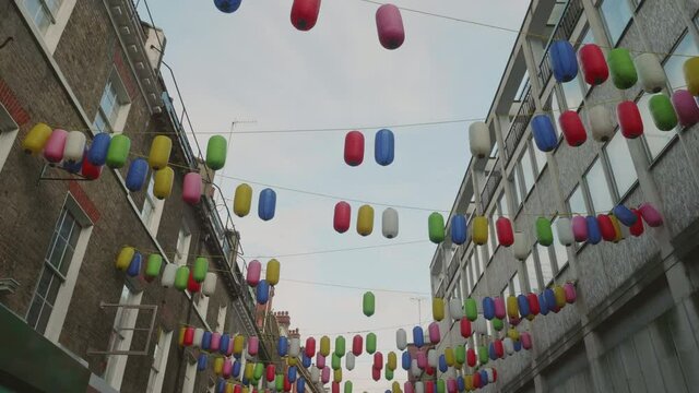 Smooth walking shot of Chinese lamps hanging between houses and dangling in the wind in Chinatown, London.