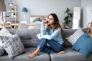 Obraz premium Upset young woman thinking about problem, sitting alone on couch at home.