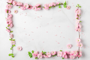 Frame made of spring pink cherry blossom branches on white marble background. Flat lay. Holiday or wedding layout