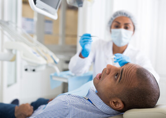 Hispanic male patient sitting in chair in dental office receiving treatment from dentist