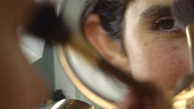 girl putting on makeup with brush adding blush bronzer on her face. Cosmetic concept. mirror close up