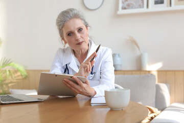 Older woman doctor therapist wearing headset video call talking to web camera consulting virtual patient online by video conference call chat.