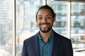 Headshot portrait of smiling young African American businessman in suit pose in own modern office....