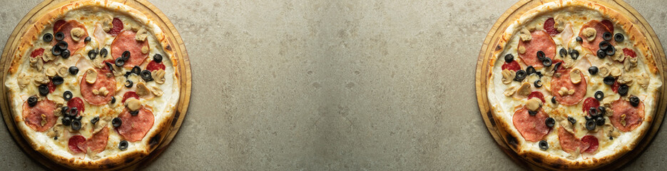 Two small pizzas with salami and olives on a gray background on both sides. Banner for a pizzeria.