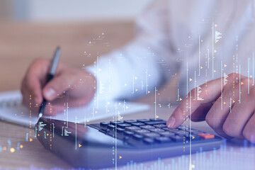 A trader computing historic data to predict stock market behavior. Internet trading concept. Forex and financial hologram chart over the desk and calculator.