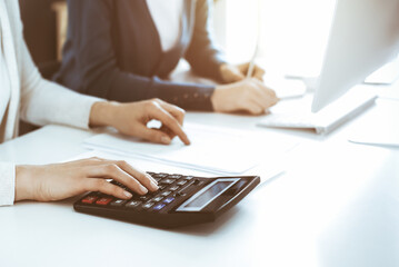 Accountant checking financial statement or counting by calculator income for tax form, hands close-up. Business woman sitting and working with colleague at the desk in office. Audit concept